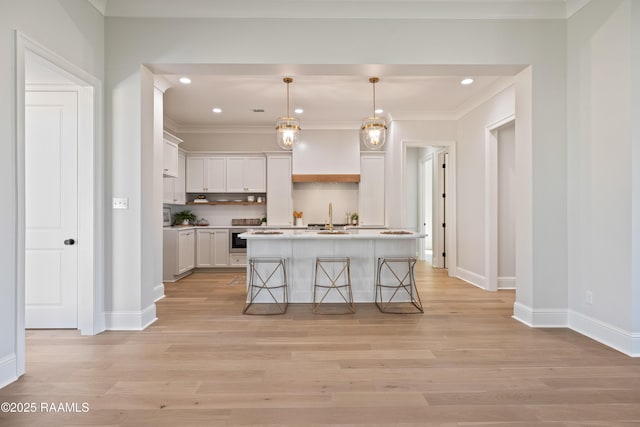 kitchen featuring a breakfast bar area, hanging light fixtures, a kitchen island with sink, white cabinetry, and a sink