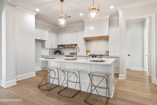 kitchen featuring light countertops, hanging light fixtures, a center island with sink, and white cabinetry