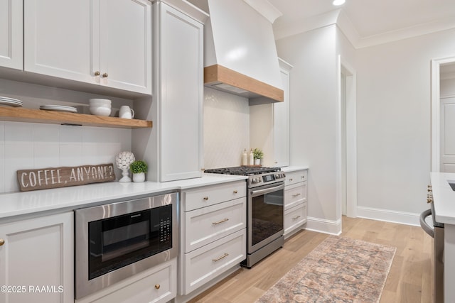 kitchen with custom exhaust hood, light countertops, white cabinets, gas range, and built in microwave