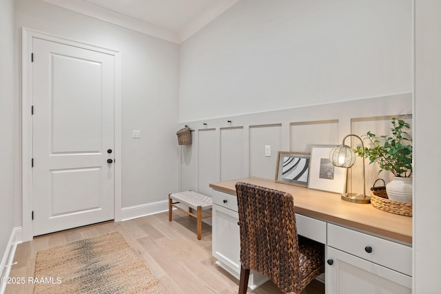 office space with light wood-type flooring, built in study area, crown molding, and a decorative wall