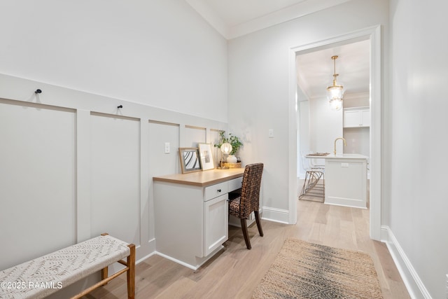 office space with light wood-style flooring, baseboards, crown molding, and built in study area