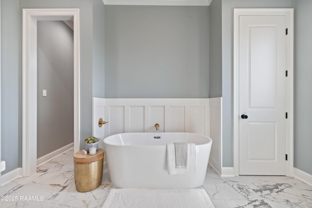 bathroom featuring marble finish floor, a freestanding bath, a decorative wall, wainscoting, and baseboards