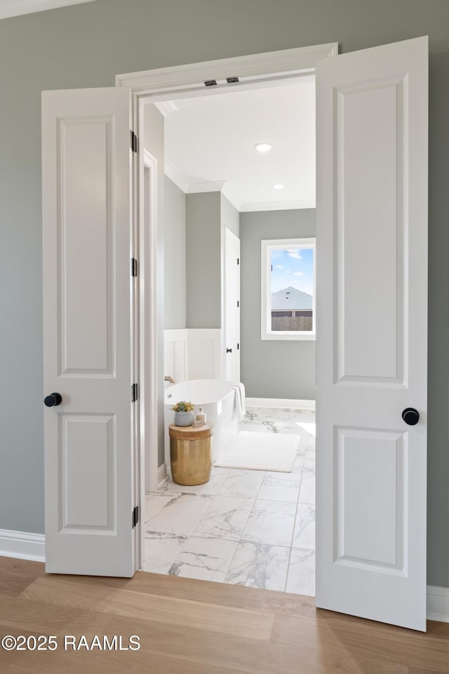 bathroom featuring ornamental molding, marble finish floor, a freestanding tub, and baseboards