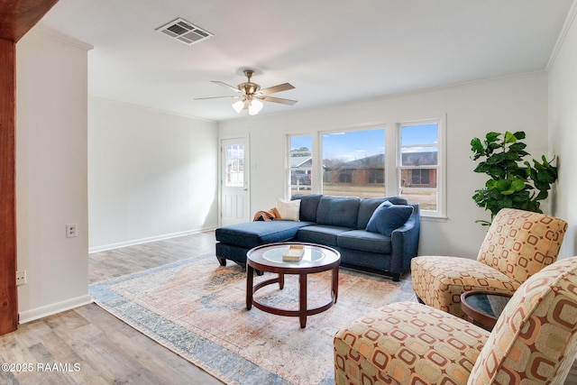 living area with ceiling fan, visible vents, baseboards, light wood-style floors, and ornamental molding