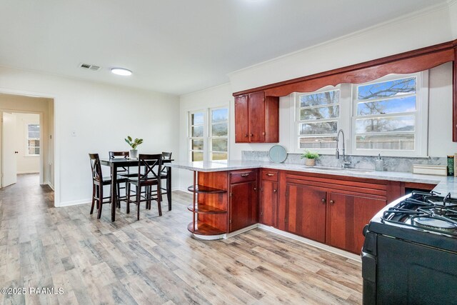 kitchen with a peninsula, a sink, visible vents, light countertops, and light wood finished floors