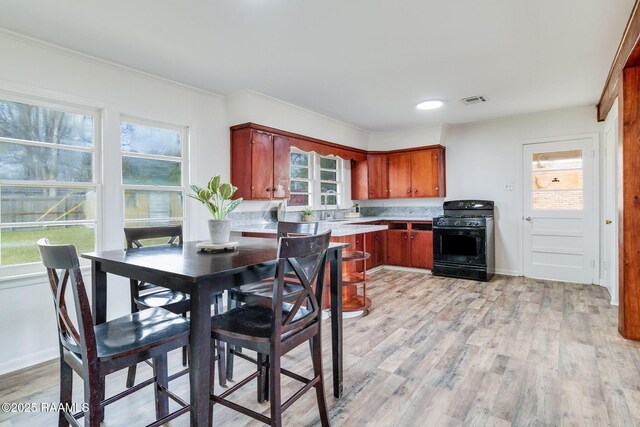 kitchen with black gas range, light wood finished floors, visible vents, ornamental molding, and light countertops