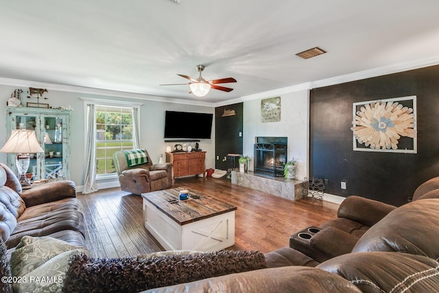 living room with crown molding, dark hardwood / wood-style floors, a premium fireplace, and ceiling fan