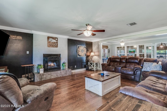 living room with dark wood-type flooring, ceiling fan, a high end fireplace, and crown molding