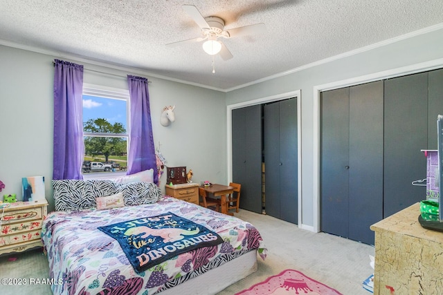 bedroom featuring ornamental molding, ceiling fan, multiple closets, light carpet, and a textured ceiling