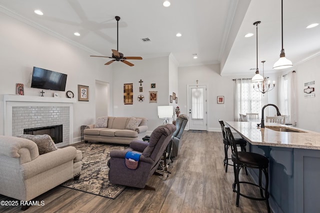 living room featuring hardwood / wood-style floors, ceiling fan with notable chandelier, sink, crown molding, and a brick fireplace