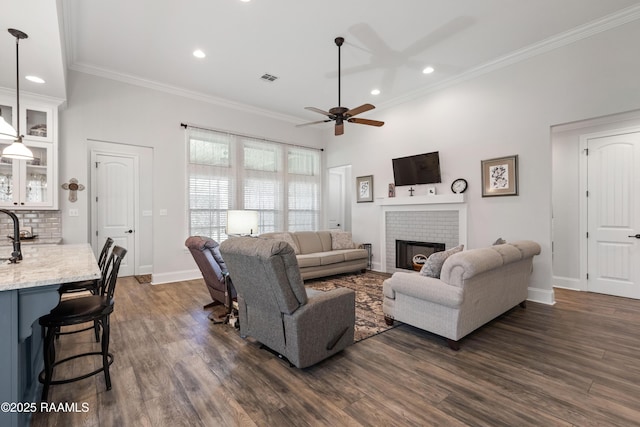 living room featuring ceiling fan, ornamental molding, dark hardwood / wood-style floors, and a brick fireplace