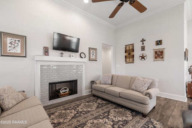 living room with dark wood-type flooring, ceiling fan, ornamental molding, and a brick fireplace