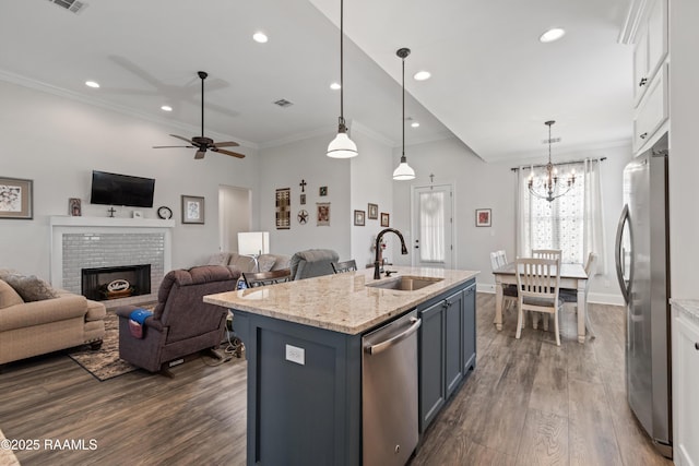 kitchen with white cabinetry, light stone counters, hanging light fixtures, appliances with stainless steel finishes, and a kitchen island with sink