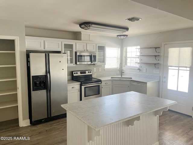 kitchen with appliances with stainless steel finishes, a breakfast bar, white cabinetry, sink, and a center island