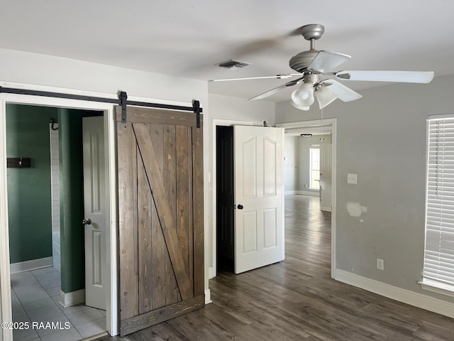 unfurnished bedroom featuring ceiling fan, a barn door, and dark hardwood / wood-style flooring