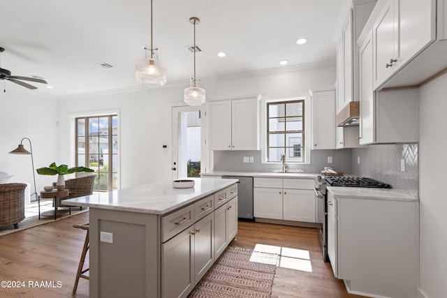 kitchen with white cabinetry, a center island, hanging light fixtures, ornamental molding, and appliances with stainless steel finishes