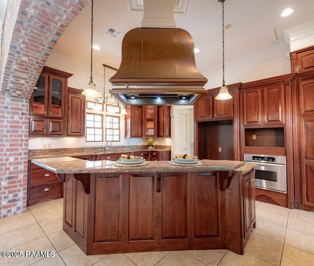 kitchen with light stone counters, a kitchen island, pendant lighting, island exhaust hood, and oven