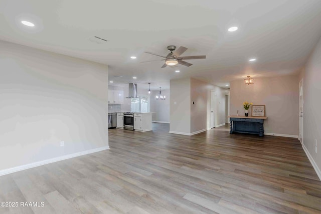 unfurnished living room with ceiling fan with notable chandelier and light hardwood / wood-style floors