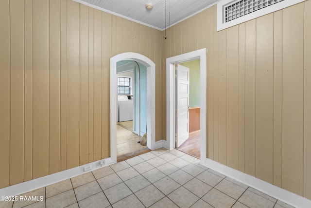 tiled empty room with washer / dryer, wooden walls, and ornamental molding