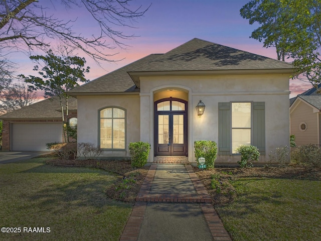 view of front of property with stucco siding, french doors, a yard, an attached garage, and a shingled roof