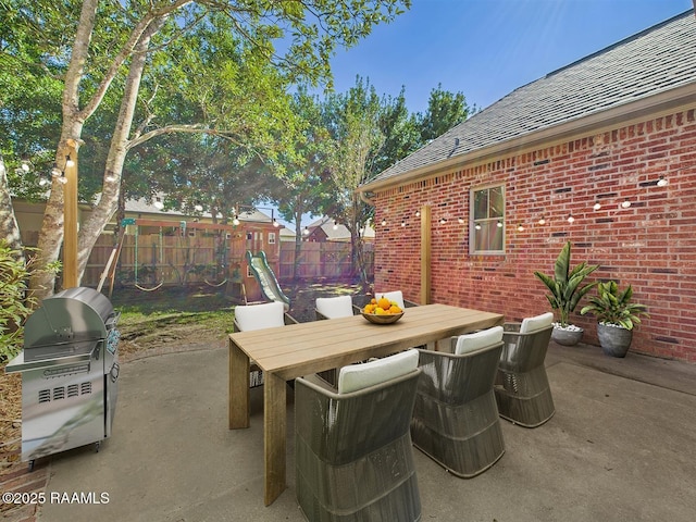 view of patio featuring outdoor dining area, a grill, a playground, and a fenced backyard