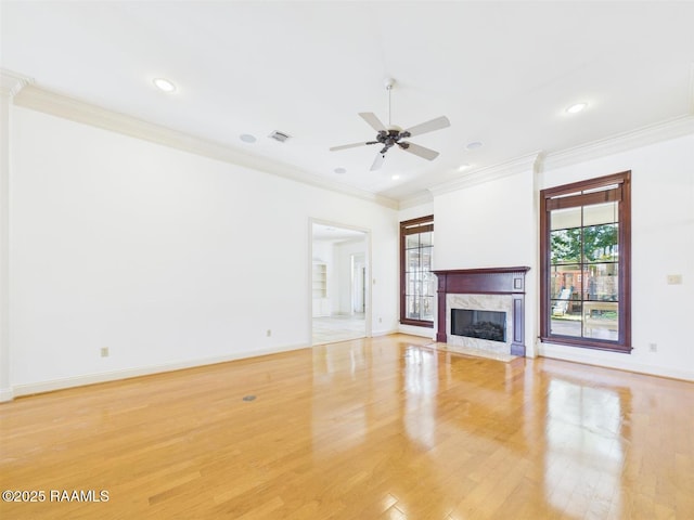 unfurnished living room featuring light wood finished floors, baseboards, a premium fireplace, ornamental molding, and a ceiling fan