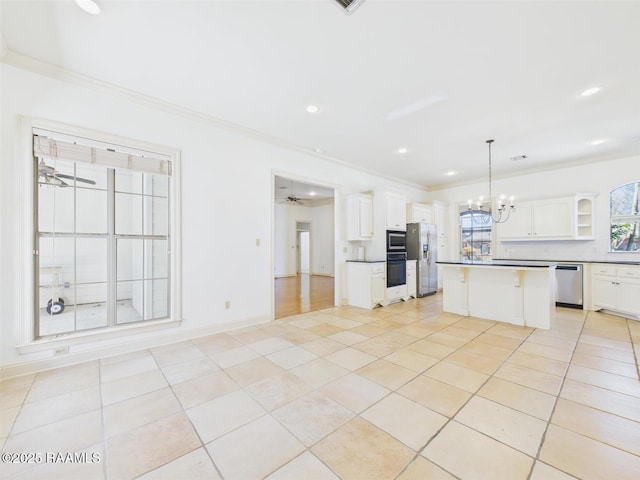 kitchen with a kitchen island, ornamental molding, white cabinets, appliances with stainless steel finishes, and ceiling fan with notable chandelier