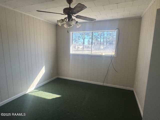 carpeted empty room featuring crown molding, ceiling fan, and wood walls