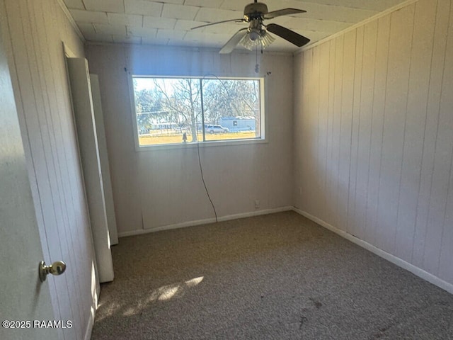 unfurnished room with carpet flooring, ceiling fan, and wood walls