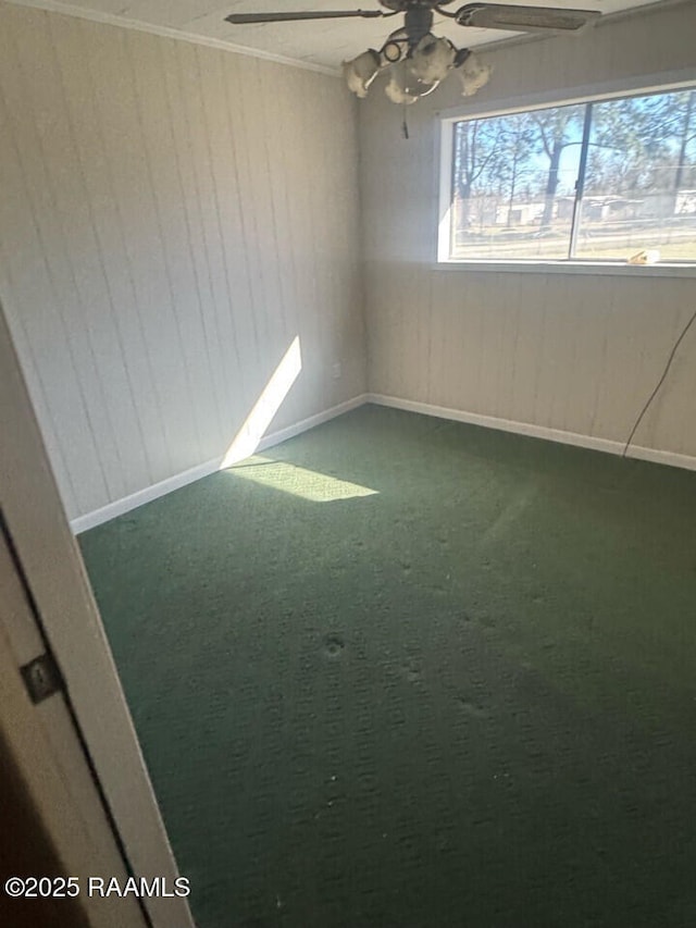 carpeted empty room featuring crown molding, wooden walls, and ceiling fan