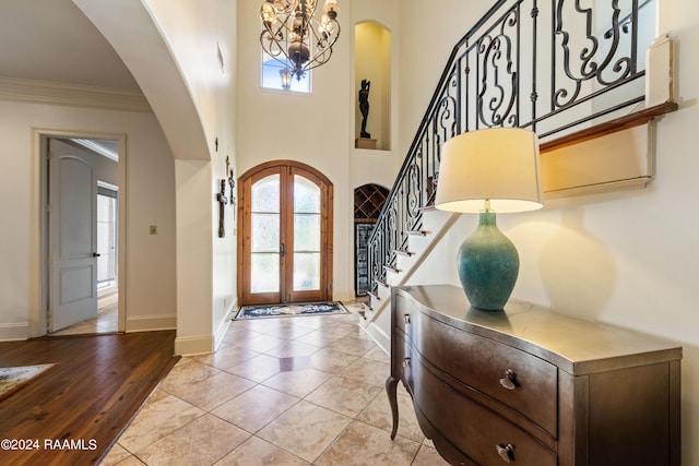 entrance foyer with a high ceiling, ornamental molding, light tile patterned floors, a notable chandelier, and french doors