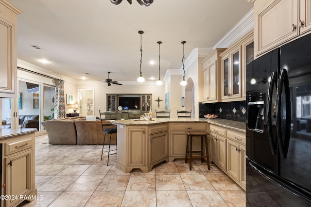 kitchen featuring hanging light fixtures, ornamental molding, kitchen peninsula, light stone countertops, and black refrigerator with ice dispenser