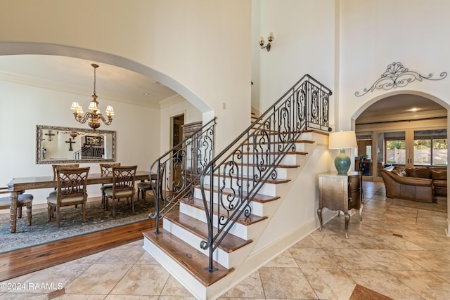 staircase featuring crown molding, a towering ceiling, and a notable chandelier