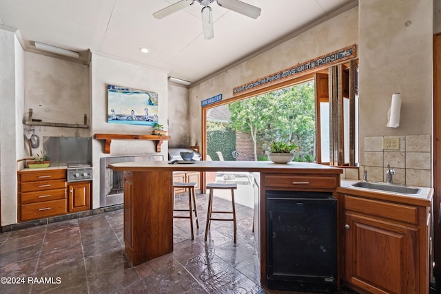 kitchen with sink, a breakfast bar area, ceiling fan, ornamental molding, and beverage cooler