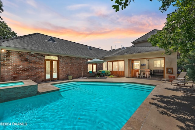 pool at dusk with exterior bar, a patio, and an in ground hot tub