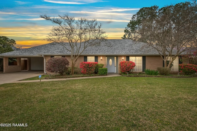 ranch-style home with brick siding, an attached carport, a shingled roof, and a yard