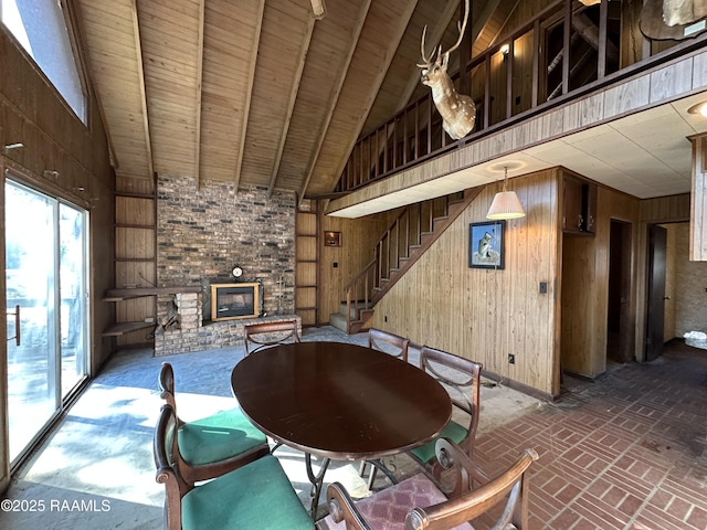 unfurnished dining area featuring high vaulted ceiling, wooden ceiling, wooden walls, and a brick fireplace