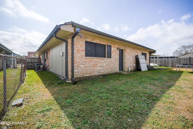 back of house with central AC, a trampoline, and a lawn