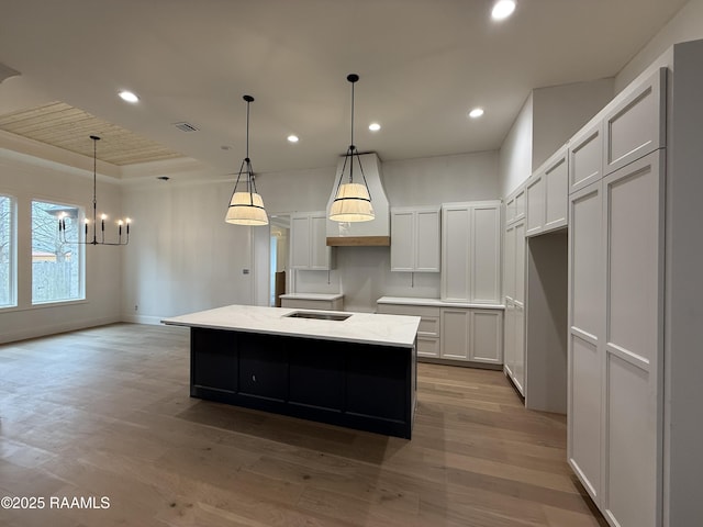 kitchen featuring white cabinetry, light stone counters, a center island with sink, pendant lighting, and light hardwood / wood-style floors