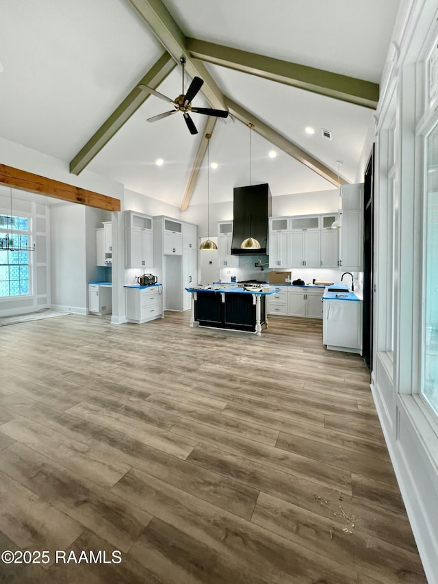 unfurnished living room featuring ceiling fan, sink, beam ceiling, and hardwood / wood-style floors