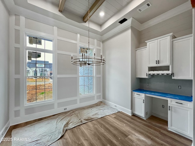 kitchen featuring built in desk, white cabinets, hanging light fixtures, beam ceiling, and light hardwood / wood-style flooring