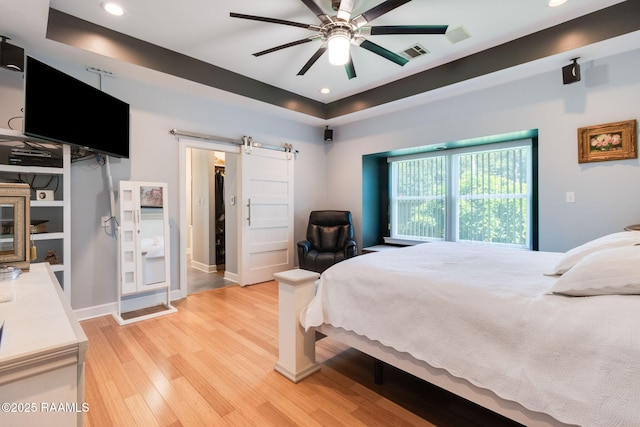 bedroom featuring ceiling fan, light hardwood / wood-style floors, a barn door, and a raised ceiling