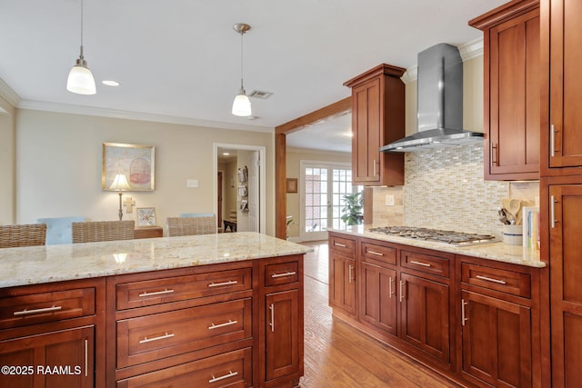 kitchen featuring pendant lighting, wall chimney range hood, crown molding, and stainless steel gas stovetop