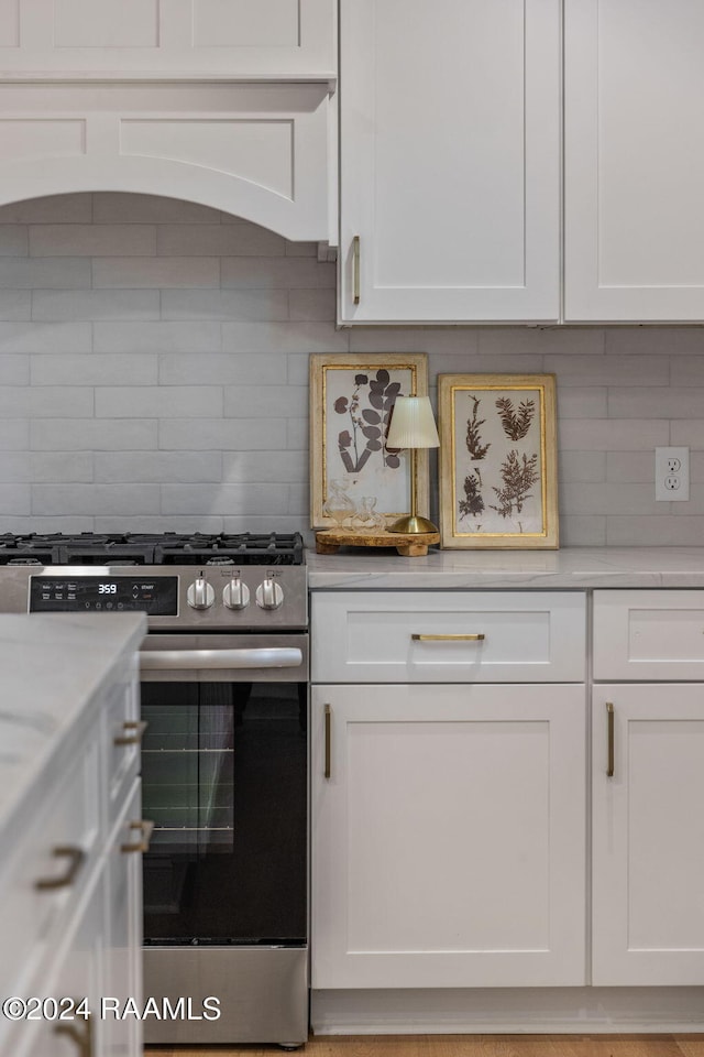 kitchen with white cabinetry, stainless steel range with gas stovetop, custom range hood, and backsplash