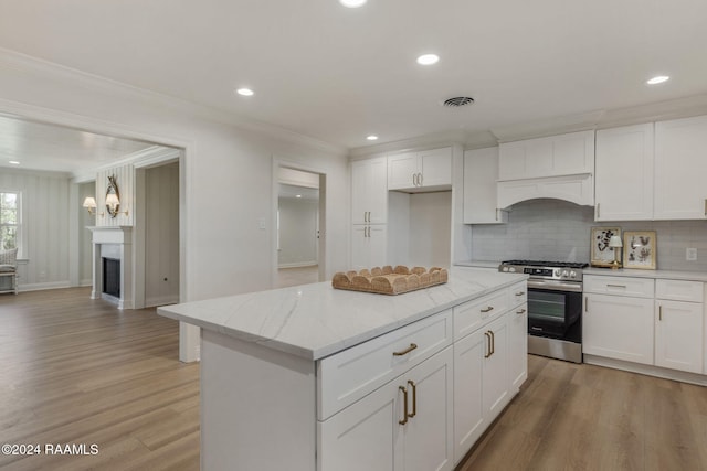 kitchen featuring white cabinetry, light stone counters, ornamental molding, and gas stove