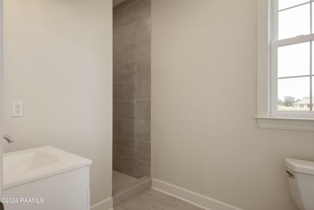 bathroom with a tile shower, vanity, tile patterned floors, and toilet