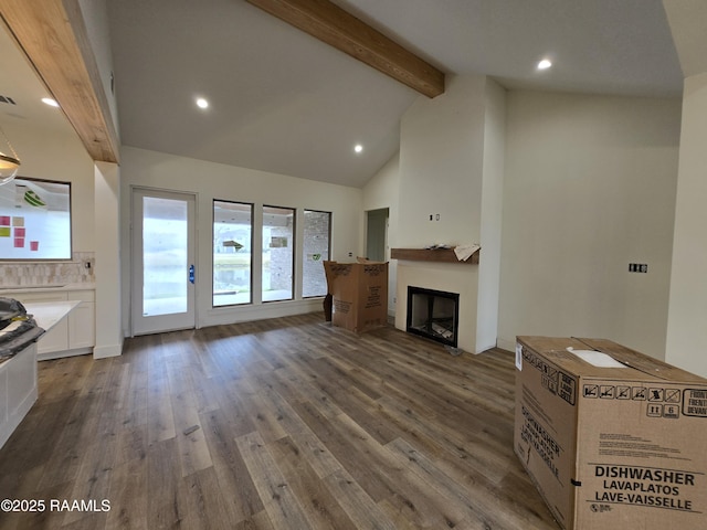 unfurnished living room with a healthy amount of sunlight, a fireplace, beamed ceiling, and wood finished floors