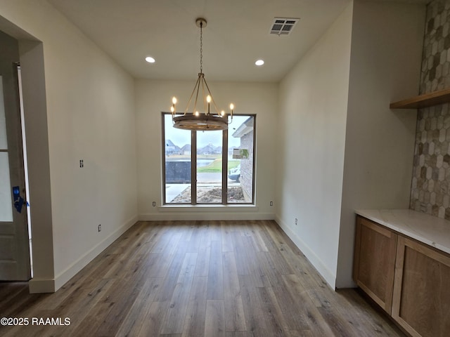 unfurnished dining area with wood-type flooring and an inviting chandelier