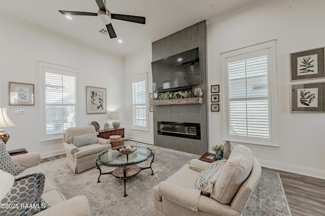 living room with hardwood / wood-style flooring, crown molding, a large fireplace, and ceiling fan