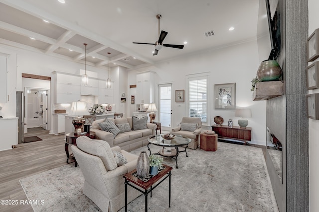 living room with a towering ceiling, coffered ceiling, ceiling fan, light hardwood / wood-style floors, and beam ceiling